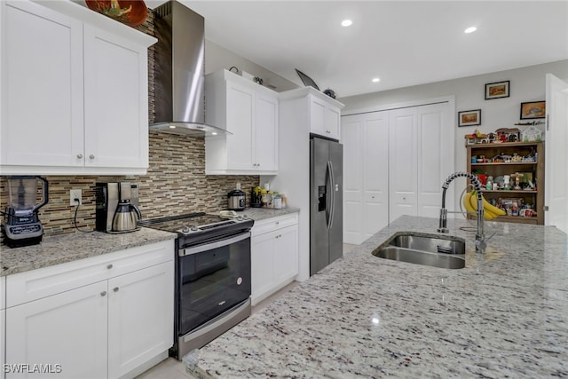 kitchen featuring decorative backsplash, wall chimney exhaust hood, appliances with stainless steel finishes, light stone countertops, and sink