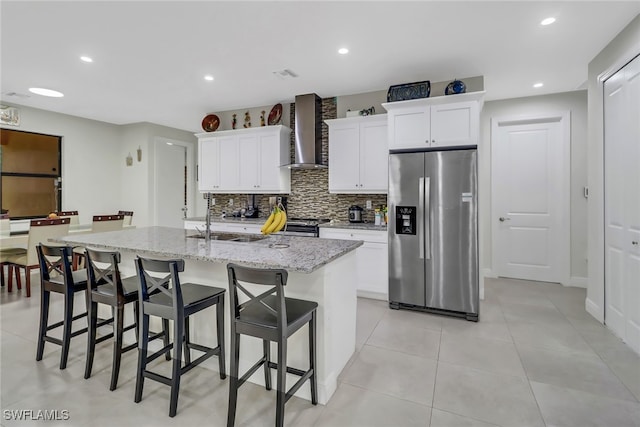 kitchen with appliances with stainless steel finishes, decorative backsplash, a center island with sink, and wall chimney range hood