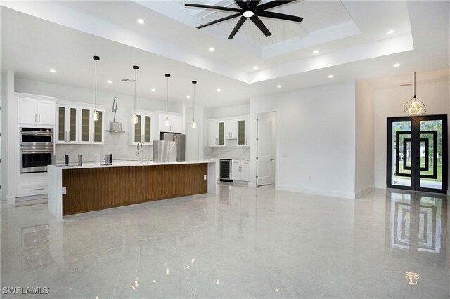 kitchen featuring appliances with stainless steel finishes, a spacious island, a raised ceiling, ceiling fan, and hanging light fixtures