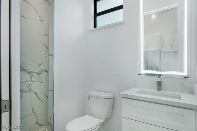 bathroom with toilet, a tile shower, and vanity