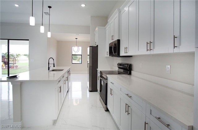 kitchen with white cabinetry, decorative light fixtures, an island with sink, sink, and appliances with stainless steel finishes