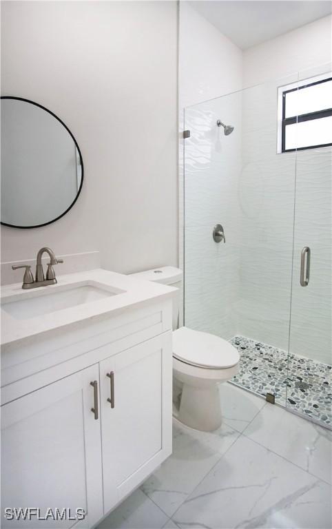 bathroom featuring toilet, marble finish floor, a shower stall, and vanity