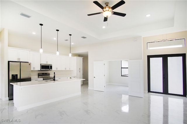 kitchen with appliances with stainless steel finishes, a tray ceiling, an island with sink, white cabinetry, and ceiling fan