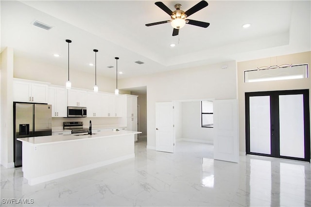 kitchen featuring a center island with sink, visible vents, a raised ceiling, appliances with stainless steel finishes, and white cabinetry