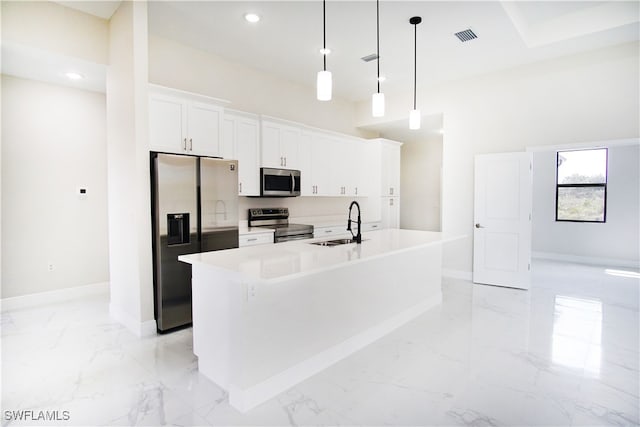 kitchen with white cabinets, decorative light fixtures, appliances with stainless steel finishes, sink, and an island with sink