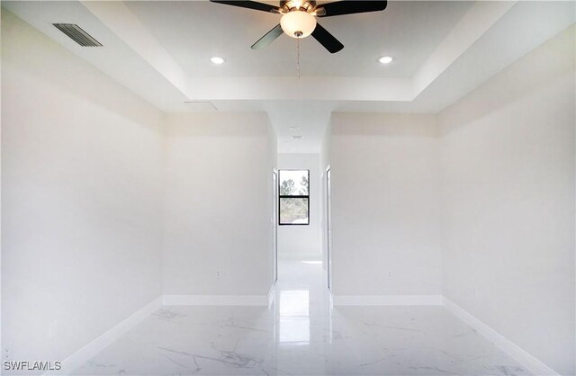 spare room featuring a tray ceiling, marble finish floor, a ceiling fan, and visible vents