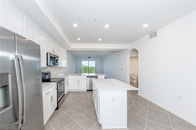 kitchen with light tile patterned flooring, appliances with stainless steel finishes, a kitchen island, and white cabinets