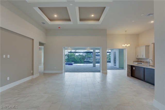 interior space with coffered ceiling, sink, a chandelier, white cabinetry, and a towering ceiling