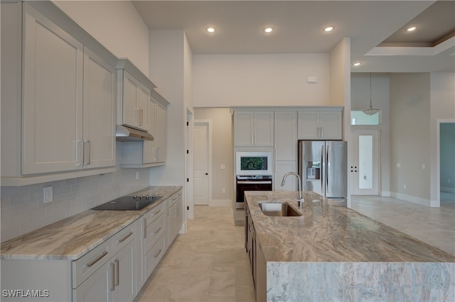 kitchen featuring a center island with sink, stainless steel fridge with ice dispenser, gray cabinets, black electric stovetop, and sink