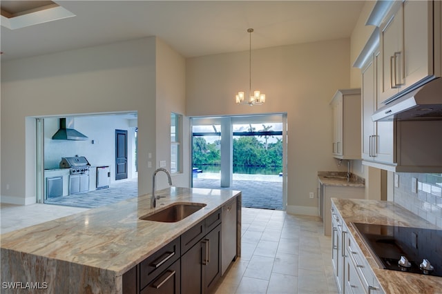 kitchen with wall chimney range hood, hanging light fixtures, a high ceiling, a notable chandelier, and sink