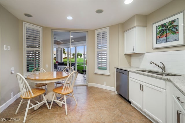 kitchen with a sink, white cabinets, stainless steel dishwasher, backsplash, and light stone countertops