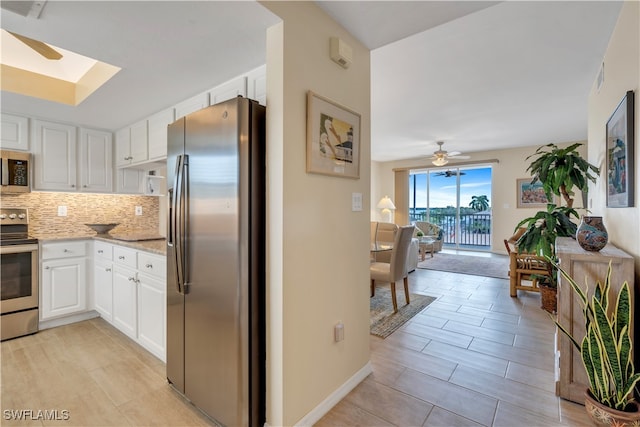 kitchen featuring white cabinets, ceiling fan, decorative backsplash, a skylight, and appliances with stainless steel finishes