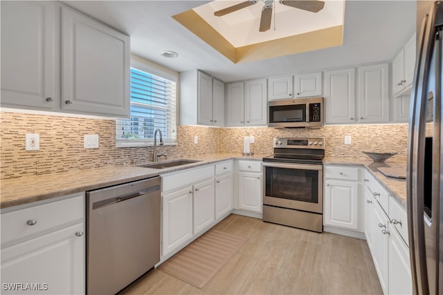 kitchen with stainless steel appliances, a tray ceiling, white cabinets, and sink