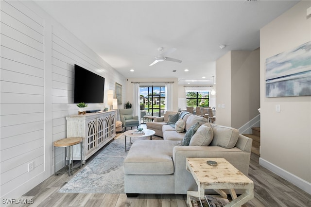 living room with light hardwood / wood-style flooring, wood walls, and ceiling fan