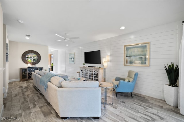 living room with light hardwood / wood-style flooring, ceiling fan, and wood walls