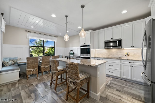 kitchen with light stone counters, stainless steel appliances, light hardwood / wood-style floors, white cabinetry, and a center island with sink