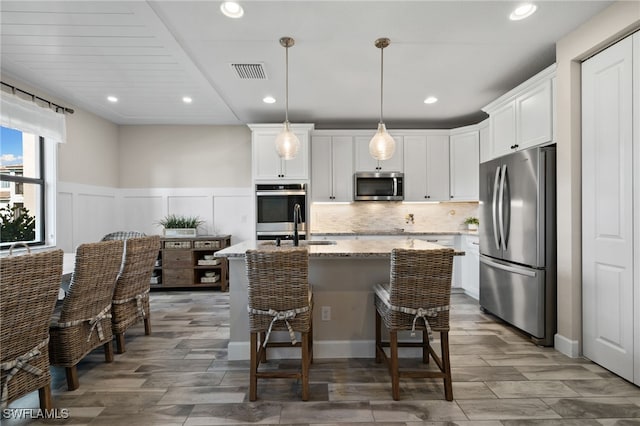 kitchen featuring an island with sink, light stone countertops, appliances with stainless steel finishes, a breakfast bar area, and white cabinets