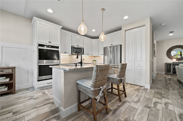 kitchen with light wood-type flooring, white cabinetry, light stone countertops, a breakfast bar, and appliances with stainless steel finishes