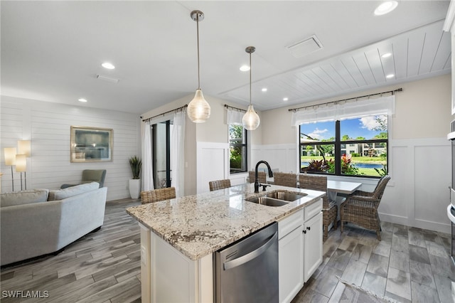 kitchen featuring a kitchen island with sink, light stone counters, sink, stainless steel dishwasher, and white cabinets