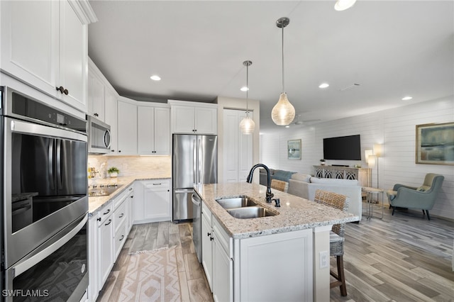 kitchen featuring appliances with stainless steel finishes, light hardwood / wood-style floors, white cabinetry, sink, and a center island with sink