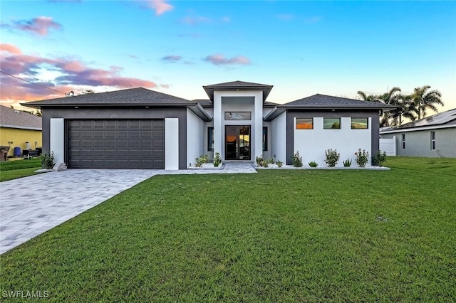 prairie-style house featuring an attached garage, a lawn, decorative driveway, and stucco siding