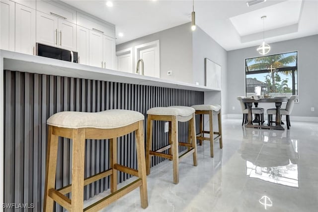 kitchen featuring visible vents, white cabinetry, baseboards, a tray ceiling, and pendant lighting