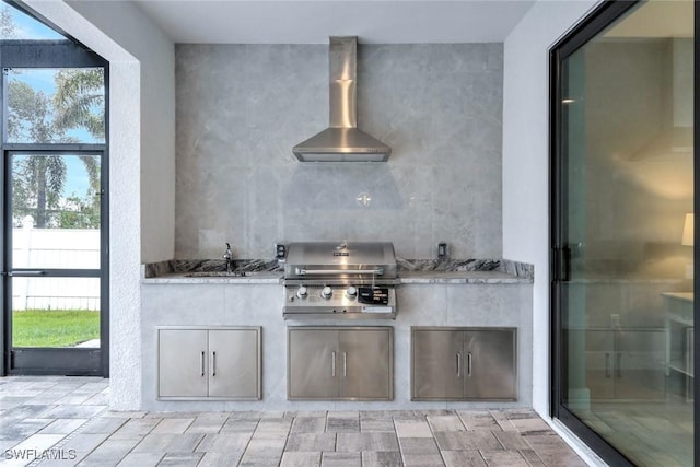 kitchen with a healthy amount of sunlight, a sink, backsplash, and wall chimney exhaust hood