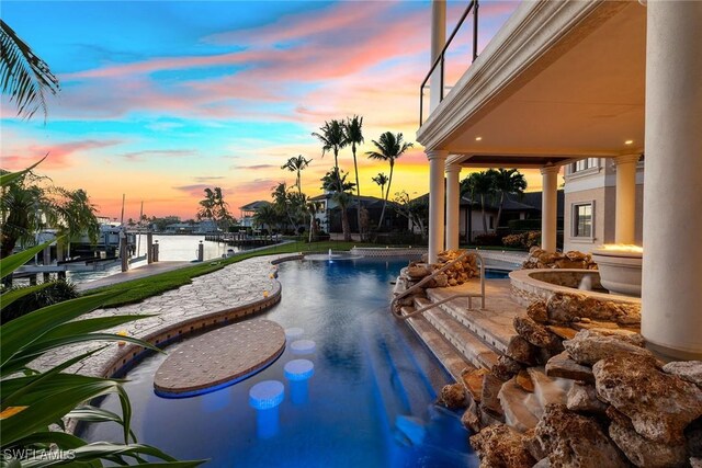 pool at dusk with a patio area, an outdoor pool, and a water view