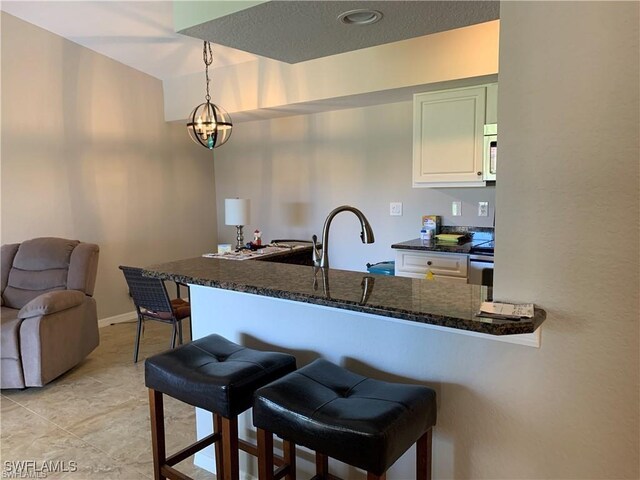 kitchen with a chandelier, a kitchen bar, pendant lighting, white cabinets, and light tile patterned floors