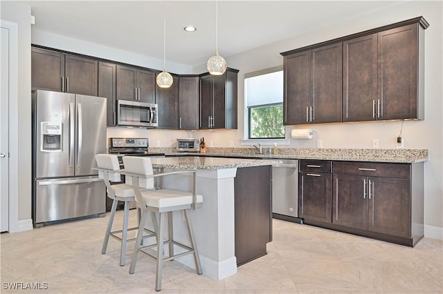 kitchen with dark brown cabinetry, light stone countertops, stainless steel appliances, a breakfast bar, and a center island