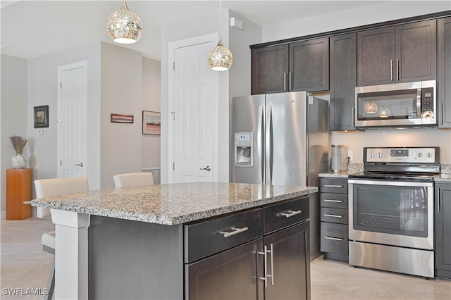 kitchen with appliances with stainless steel finishes, light stone counters, dark brown cabinetry, and hanging light fixtures