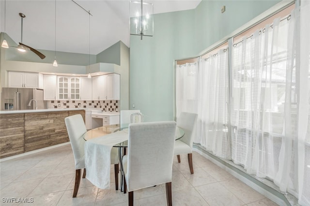 tiled dining room featuring high vaulted ceiling, ceiling fan with notable chandelier, and sink