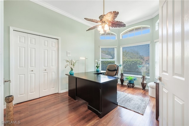 home office featuring dark wood-type flooring, ceiling fan, ornamental molding, and a towering ceiling