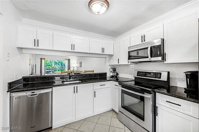 kitchen with dark stone counters, white cabinetry, light tile patterned floors, sink, and stainless steel appliances