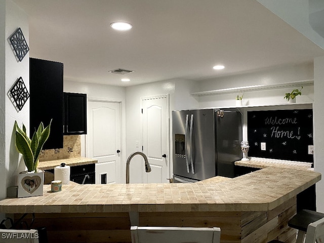 kitchen with kitchen peninsula, decorative backsplash, and stainless steel fridge with ice dispenser