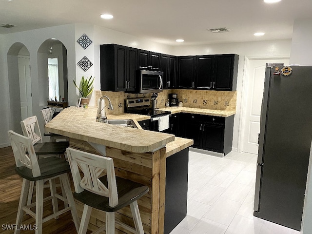 kitchen featuring decorative backsplash, light tile patterned floors, sink, kitchen peninsula, and stainless steel appliances