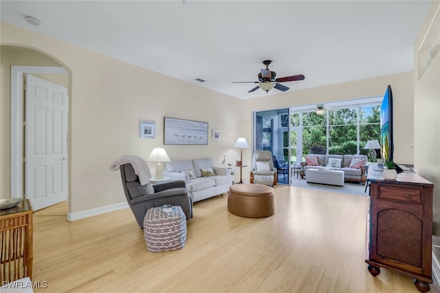 living area featuring visible vents, arched walkways, a ceiling fan, baseboards, and light wood-type flooring