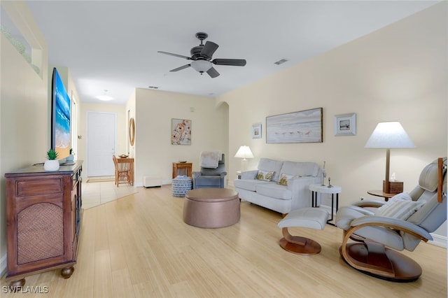 living room with arched walkways, visible vents, ceiling fan, and wood finished floors