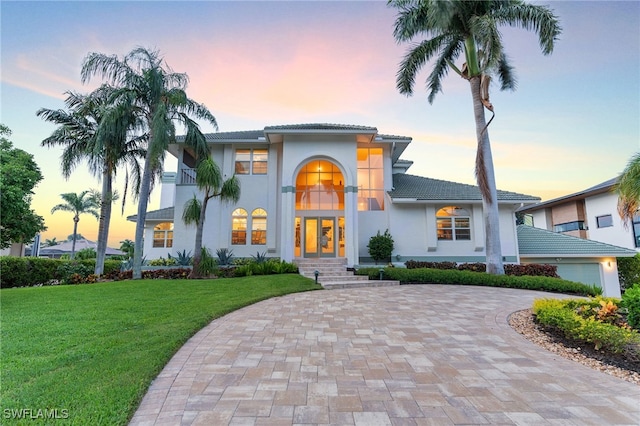 view of front of house featuring a tiled roof, decorative driveway, a lawn, and stucco siding