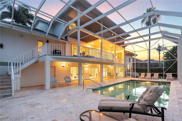 pool at dusk with glass enclosure and a patio