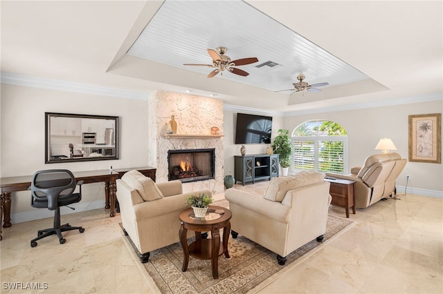 tiled living room featuring ceiling fan, a fireplace, a tray ceiling, and ornamental molding