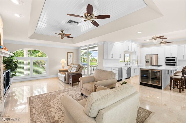 living room with ceiling fan, a raised ceiling, a healthy amount of sunlight, and light tile patterned floors