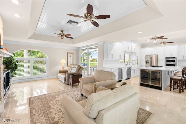 living area with a healthy amount of sunlight, marble finish floor, wine cooler, and a tray ceiling