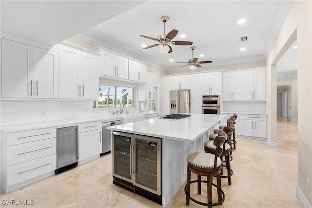 kitchen with stainless steel appliances, ceiling fan, a center island, and ornamental molding