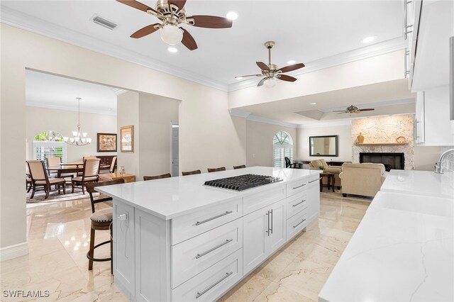 kitchen featuring ceiling fan with notable chandelier, stainless steel gas stovetop, white cabinetry, and a fireplace