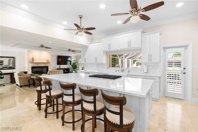 kitchen with a kitchen island, ceiling fan, a large fireplace, and white cabinets