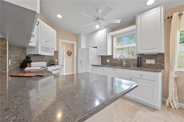 kitchen with decorative backsplash, white cabinetry, a sink, dark stone countertops, and white appliances