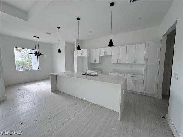 kitchen featuring sink, a center island with sink, light wood-type flooring, pendant lighting, and white cabinets