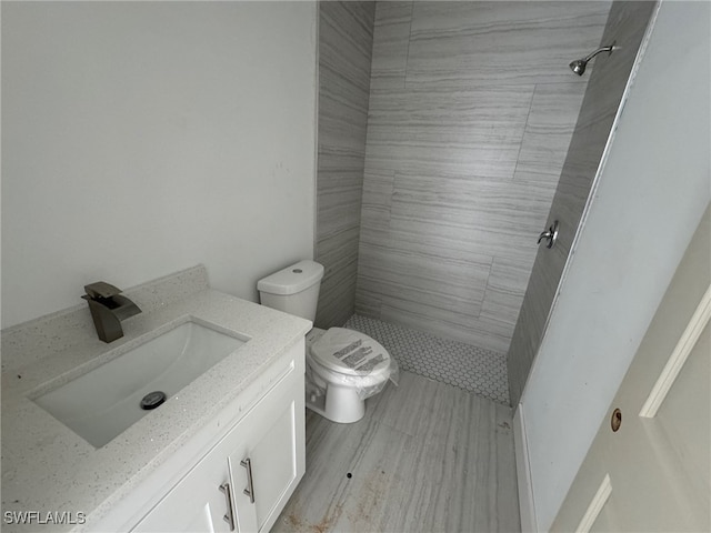 bathroom with tiled shower, toilet, and vanity