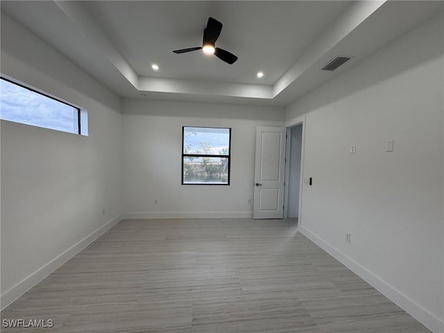 unfurnished room with a raised ceiling, a wealth of natural light, ceiling fan, and light hardwood / wood-style floors